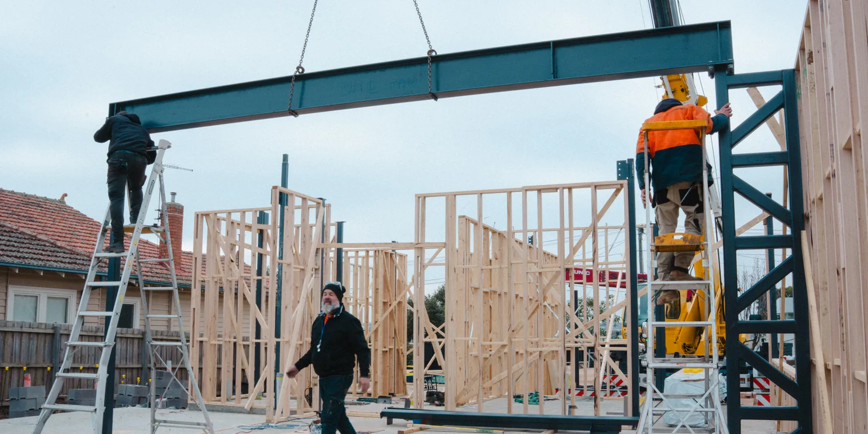 Steel beam craned into position over a timber-framed build during construction site progress filming in Melbourne
