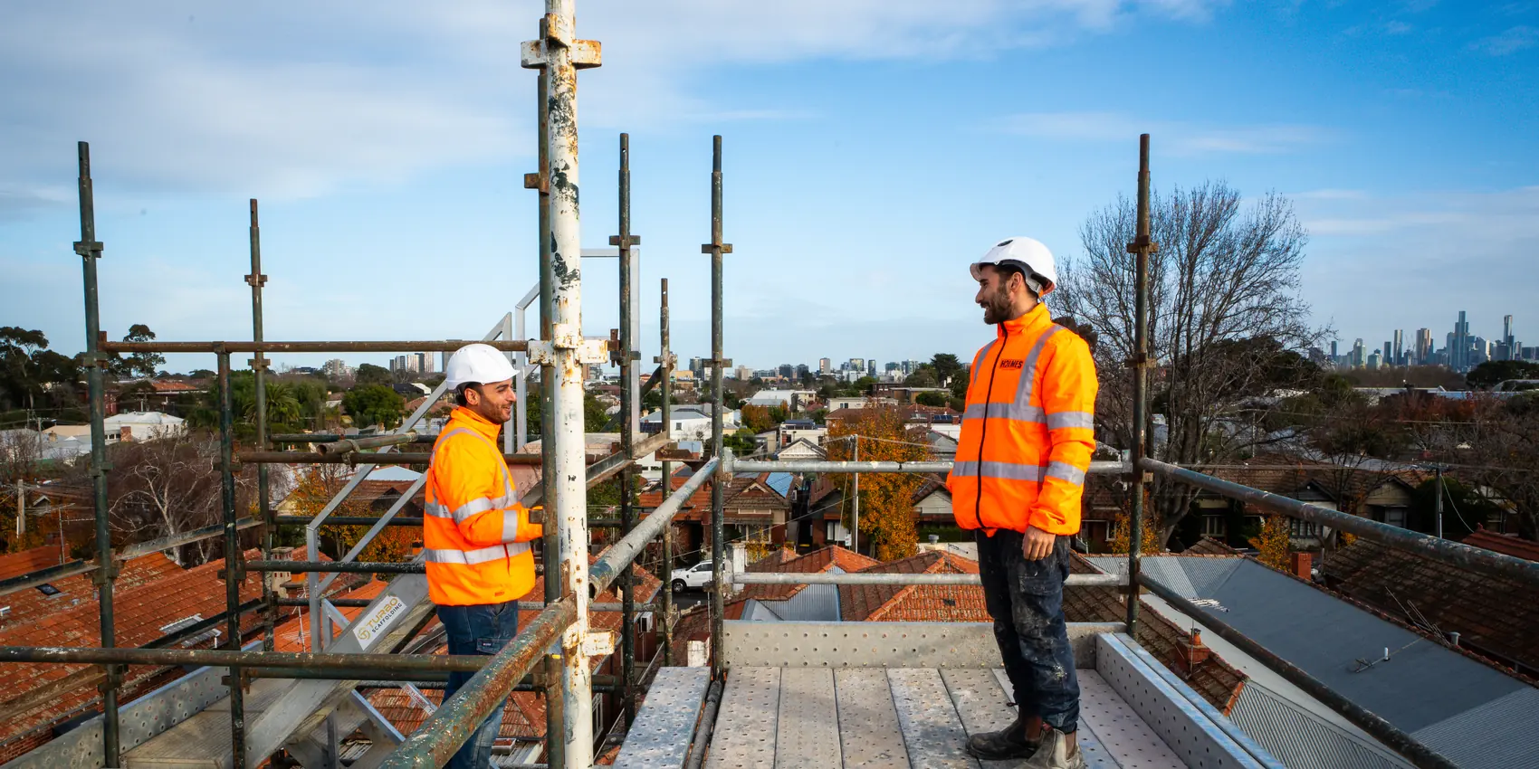 Holmes Plumbing team on the scaffold of a Prahran townhouse development with the Melbourne skyline behind