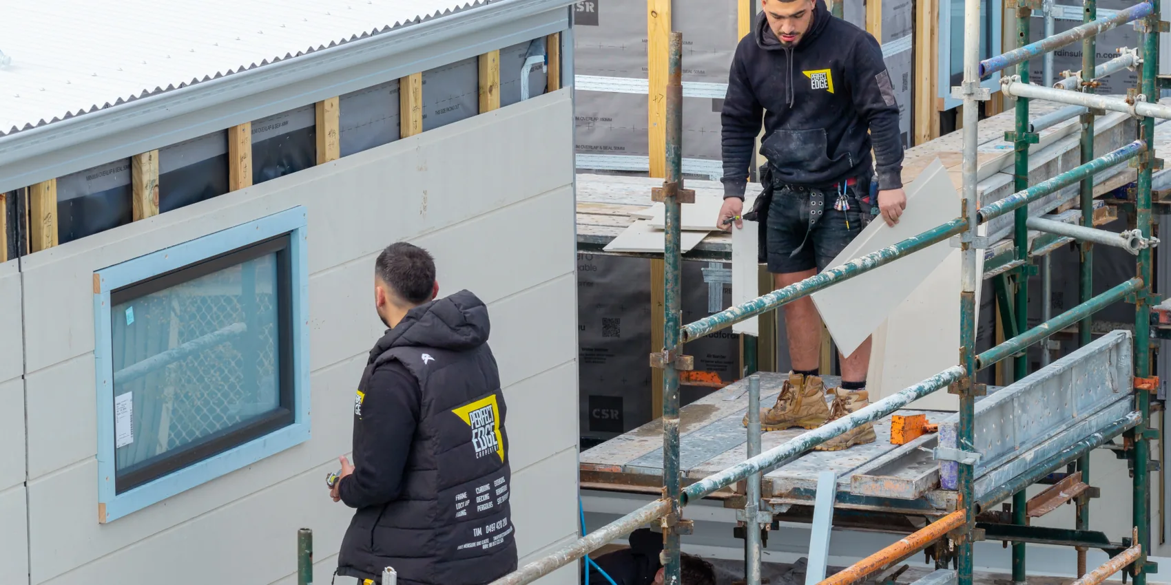 Tradespeople installing facade cladding on scaffolding during a Melbourne construction video shoot