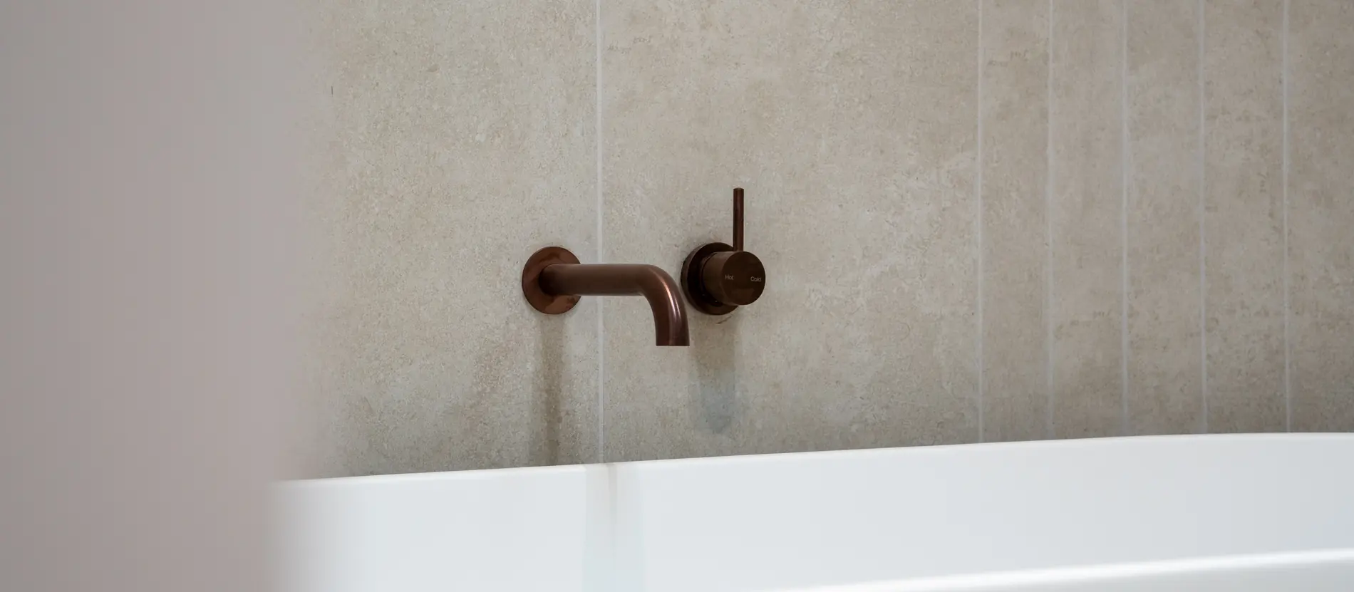 Close up of brushed bronze wall mounted tapware above a bath